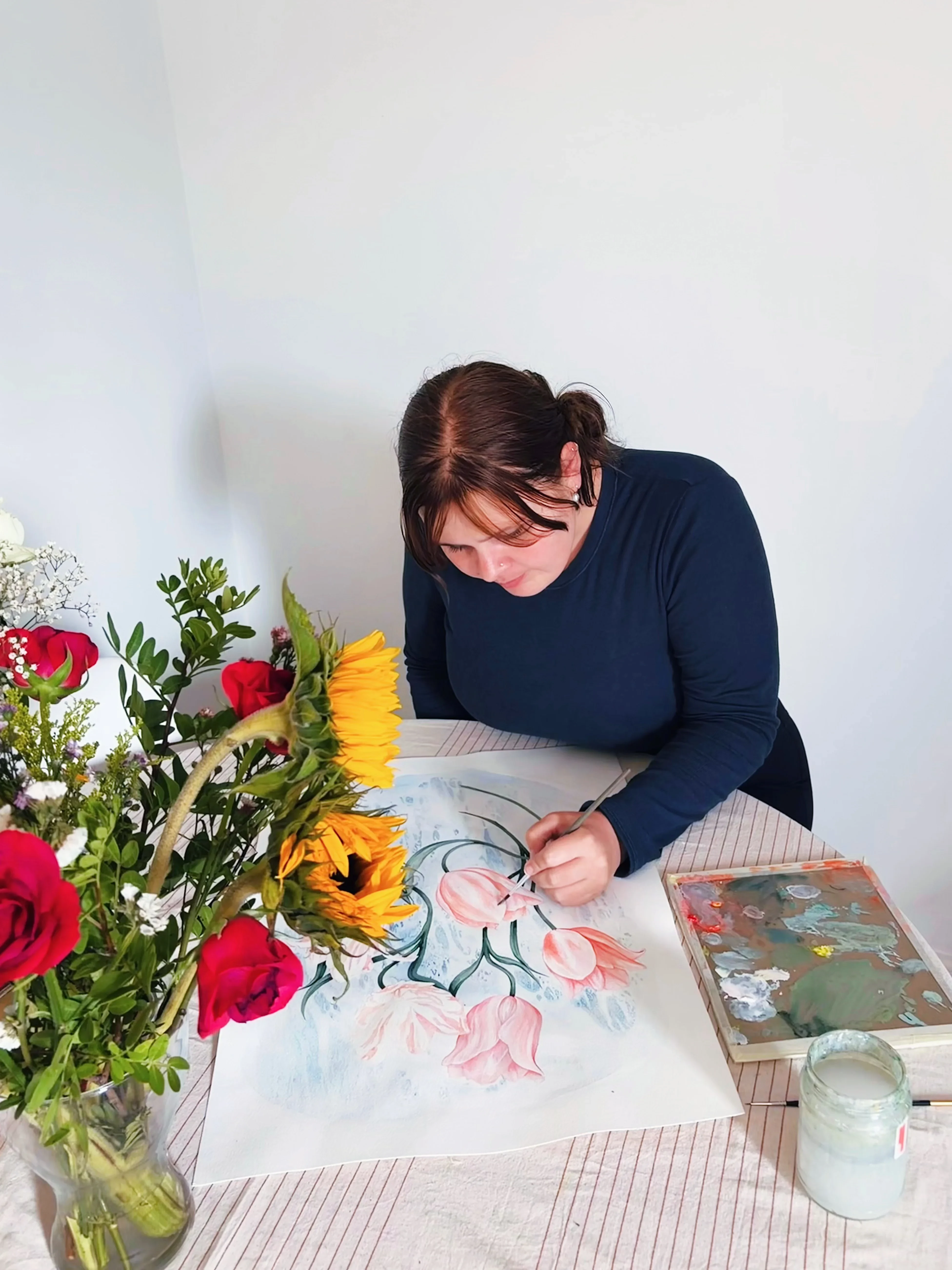 Ruby Smythe painting at a table beside a bouquet of flowers